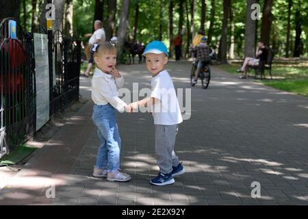 Garçon et fille marchent dans le parc en tenant les mains. Banque D'Images