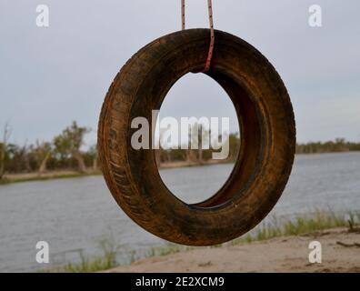 Balançoire de pneu de voiture ancienne pour les enfants à jouer sur les rives boueuses de la rivière Murray à Mildura suspendu par un morceau de corde Banque D'Images