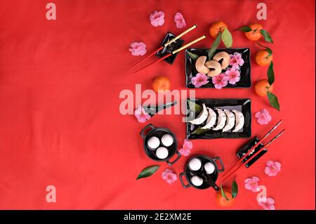 Plat Lay chinois nouvel an nourriture et boisson encore la vie. Nourriture et boissons, boulettes cuites à la vapeur, boulettes de riz Tangyuan, biscuits fortune sur plaque noire et fond rouge. Photo de haute qualité. Copier l'espace. Banque D'Images