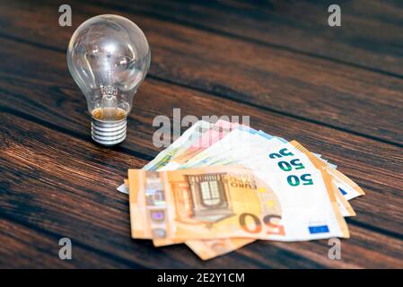 Sur fond de bois, il y a une ampoule et de l'argent sous forme de plusieurs factures. Banque D'Images