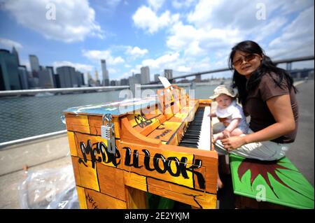 Une femme avec un bébé joue un piano dans le Brooklyn Bridge Park, dans le quartier de Brooklyn à New York, le lundi 23 juin 2010. Le piano, un de 60, fait partie d'une installation d'art qui fait le tour du monde qui fait son premier arrêt américain à New York. Le concept a mis plus de 130 pianos dans des parcs, des places et des stations de bus dans des villes de Londres à Sydney, en Australie. Photo de Mehdi Taamallah/ABACAPRESS.COM Banque D'Images