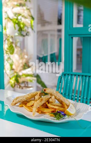 Poisson et frites avec sauce et citron, décoré de fleurs de pois papillons. Servi sur une plaque en céramique blanche. Banque D'Images