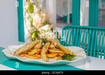 Poisson et frites avec sauce et citron, décoré de fleurs de pois papillons. Servi sur une plaque en céramique blanche. Banque D'Images