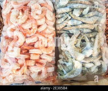 Deux grands sacs en plastique de crevettes crues et cuites congelées, sur le comptoir du marché du poisson. Banque D'Images