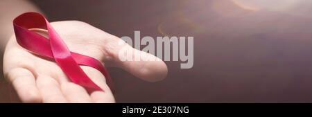 Ruban rouge dans les mains de femme sur fond sombre pour le concept de la Journée mondiale du sida. Banque D'Images