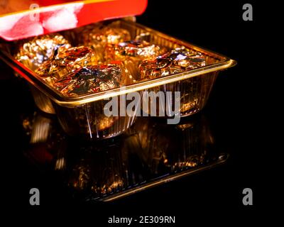 Boîte de bonbons ronds en papier d'aluminium doré sur fond noir. Chocolats emballés. Gâteau rond. Mets sucrés. Cadeau sucré. Couleur dorée. Photo de nourriture. Produit Banque D'Images