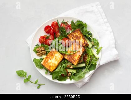 Salade fraîche d'arugula, tomates cerises, concombres et fromage rôti sur fond de pierre grise. Vue du dessus. Délicieux repas sains Banque D'Images