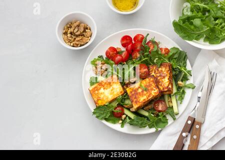 Salade fraîche d'arugula, tomates cerises, concombres et fromage rôti sur fond de pierre grise. Vue du dessus. Délicieux repas sains. Espace libre Banque D'Images