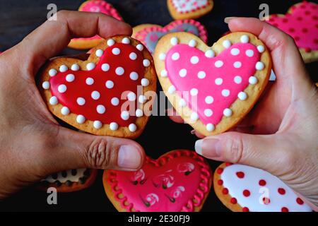 Biscuits rouges et roses pointillées en forme de coeur dans les mains de couple mettez-vous dans un tas de cookies colorés Banque D'Images