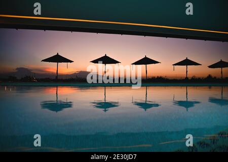 Vue sur la piscine au coucher du soleil avec silhouettes de parasol et réflexions vues depuis le toit-terrasse du Rosewood Hotel à Puebla de Zaragoza, au Mexique. Banque D'Images