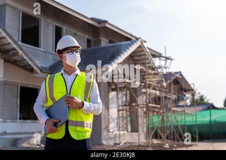 Portrait de l'architecte portant un masque tenir un ordinateur portable sur un chantier de construction, idées de construction domiciliplus et prévention de la maladie du coronavirus. Banque D'Images