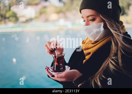 La main d'une femme tient une tasse blanche de chaud boisson lactée à la cannelle appelée sahlep de salep turc sur le Fond de l'eau ondulée et de la brumeuse Ma Banque D'Images