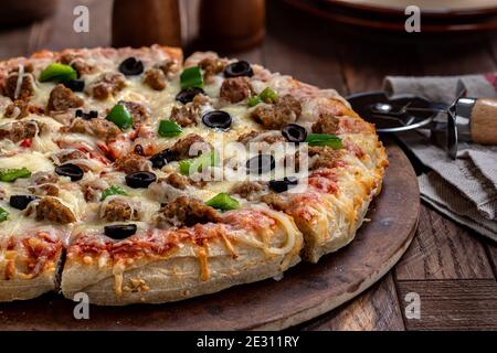 Gros plan d'une pizza avec saucisse, olives noires et poivrons verts sur une pierre à pâtisserie Banque D'Images