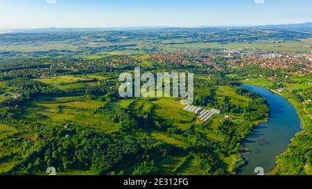 Tourné au-dessus de vert paysage vallonné avec le lac, plusieurs parcelles cultivées parmi les arbres forestiers et la ville au loin. Banque D'Images