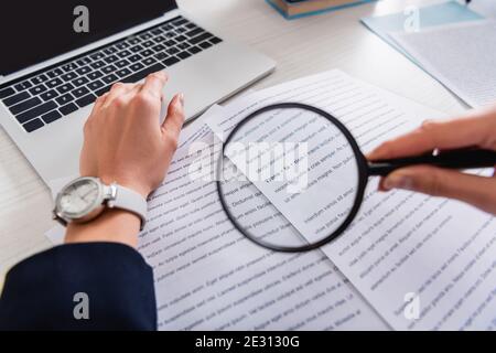 vue rognée du traducteur tenant la loupe près des documents avec texte anglais, avant-plan flou Banque D'Images