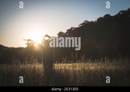 Une jeune femme danse dans l'herbe haute, rétroéclairé par le soleil couchant pendant l'heure d'or Banque D'Images