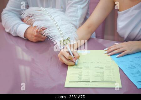 La main d'une femme signe et enregistre son mariage avec la femme qu'il aime : signe le contrat . Marié et mariée enregistrer le mariage. La femme met son signe Banque D'Images