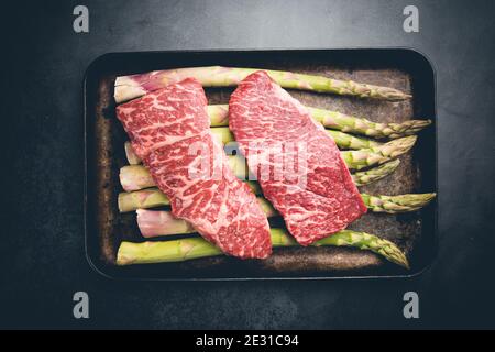 Steak cru avec asperges vertes sur plateau sur fond noir, vue de dessus Banque D'Images