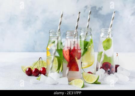 Beaucoup de bouteilles avec limonade d'été rafraîchissante avec citron vert, fraise, cerise, concombre et glace sur fond de béton gris. Banque D'Images