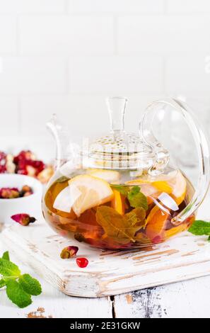 Thé aux fruits avec baies, citron, citron vert et feuilles de menthe dans une théière en verre sur fond blanc en bois clair. Mise au point sélective. Banque D'Images