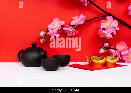 Fleur de cerisier Sakura, théière chinoise noire et Ingot d'or en verre et enveloppe rouge sur fond blanc et rouge Banque D'Images