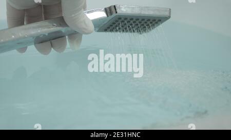 Infirmière avec des gants de protection dans les mains pour préparer une salle de bain chaude Utilisation de la pomme de douche Banque D'Images