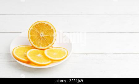 Un demi-citron mûr et trois tranches sur une assiette blanche sur une table en bois blanc. CopySpace. Banque D'Images