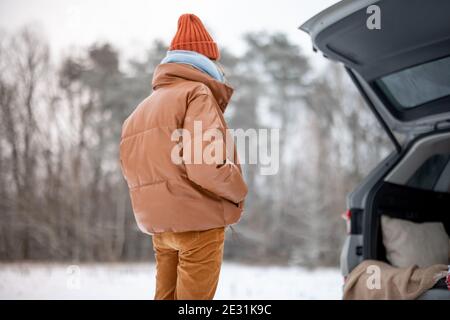 Femme avec boisson chaude restant près du coffre de voiture en hiver forêt Banque D'Images