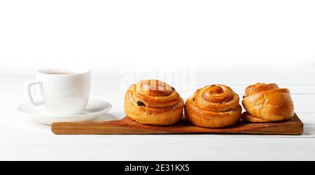 Trois petits pains aux raisins secs et une tasse de thé sur une table blanche sur fond blanc. CopySpace. Banque D'Images