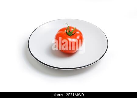 Une seule tomate brute mûre rouge fraîche sur une plaque blanche isolée sur fond blanc. Banque D'Images