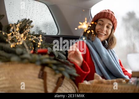 Femme souriant et regardant le sparkler en étant assise en voiture coffre Banque D'Images