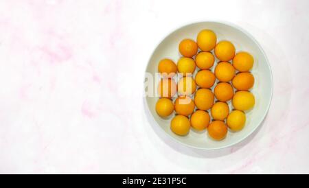 Plat de nombreux petits kumquats ronds comestibles, sur une plaque blanche. Avec un arrière-plan en marbre rose et un espace de copie sur la gauche. Banque D'Images