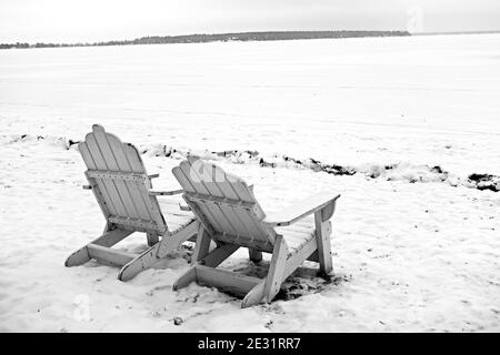 Photo en niveaux de gris de chaises de jardin en bois dans une forêt enneigée Banque D'Images