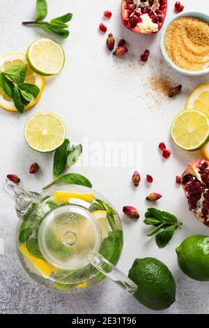 Citron frais, lime, grenade, fleurs de rose de thé séchées, thé, sucre de canne, feuilles de menthe et théière en verre sur fond gris. Ingrédients pour faire froid Banque D'Images