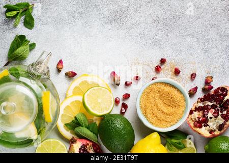 Citron frais, lime, grenade, fleurs de rose de thé séchées, thé, sucre de canne, feuilles de menthe et théière en verre sur fond gris. Ingrédients pour faire froid Banque D'Images