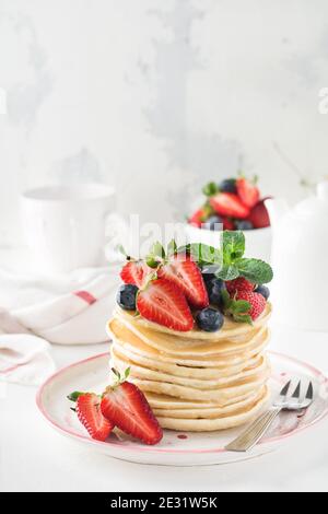 Pile de petites crêpes faites maison avec du miel, des fraises fraîches et de la sauce sur fond de bois clair. Mise au point sélective. Banque D'Images
