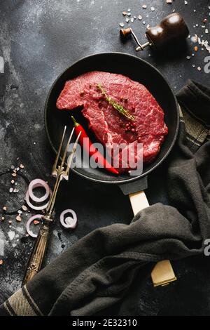 Steak de bœuf cru aux épices, oignons et piment dans une poêle en fonte pour faire frire sur fond d'ardoise sombre ou de béton. Vue de dessus. Banque D'Images