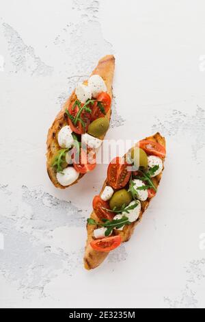 Toasts de bruschetta de Caprese avec tomates cerises, mozzarella, olives et basilic sur fond blanc ancien clair. Vue de dessus. Banque D'Images