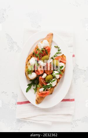 Toasts de bruschetta de Caprese avec tomates cerises, mozzarella, olives et basilic sur fond blanc ancien clair. Vue de dessus. Banque D'Images