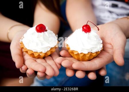 petits gâteaux à la crème. Deux gâteaux de cerise sur le dessus. Gâteau à la main Banque D'Images