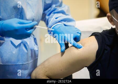 Détails sur un homme qui reçoit une injection intramusculaire avec le vaccin contre le SRAS-COV-2 dans un hôpital par un travailleur médical. Banque D'Images