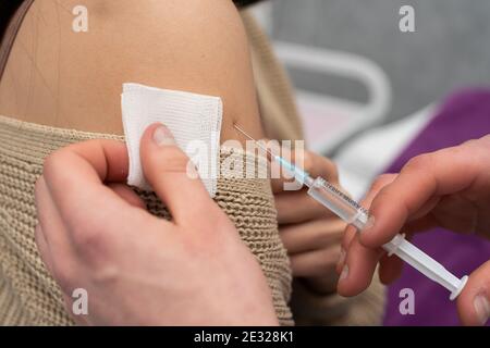 Administration du vaccin COVID19 en insérant une aiguille dans le bras du patient et en comprimant le contenu du vaccin hors de la seringue. Mains de médecin masculin. Banque D'Images