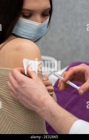 Administration du vaccin COVID19 en insérant une aiguille dans le bras du patient et en comprimant le contenu du vaccin hors de la seringue. Mains de médecin masculin. Banque D'Images