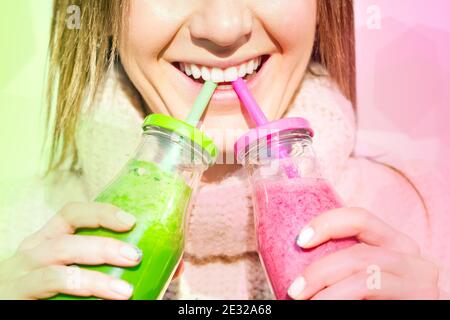 Femme souriante buvant à partir de 2 bouteilles de rose et de vert smoothie maison Banque D'Images