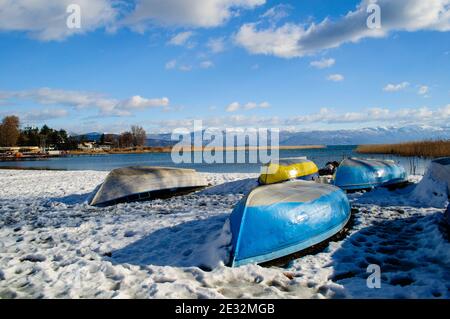 Le long de la rive du lac en hiver. Plantes et roseaux couverts de neige, bateaux rentournés par l'eau. Banque D'Images