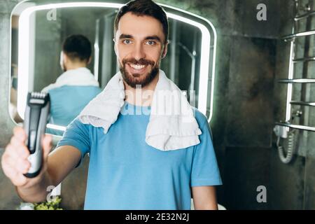 Jeune homme souriant avec une serviette présentant un nouveau rasoir tôt le matin dans la salle de bains. Banque D'Images