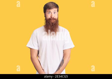 Beau jeune homme à tête rouge avec une longue barbe portant une chemise blanche décontractée puffant les joues avec le visage drôle. Bouche gonflée avec de l'air, expression folle. Banque D'Images