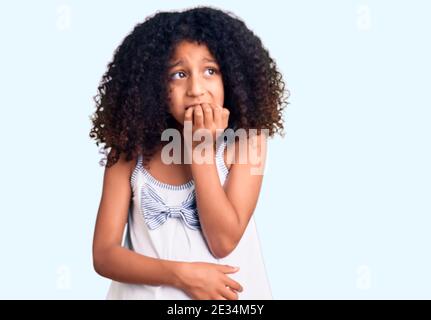 Enfant afro-américain aux cheveux bouclés portant des vêtements décontractés qui ont l'air stressés et nerveux avec les mains sur la bouche piquant les ongles. Problème d'anxiété. Banque D'Images