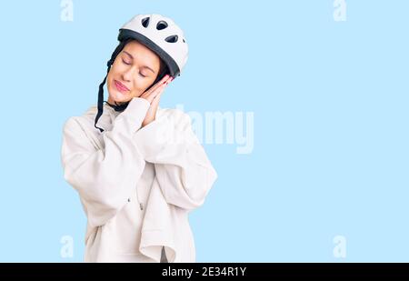 Belle brune jeune femme portant un casque de vélo et des vêtements sportifs dormir fatigué rêvant et posant avec les mains ensemble tout en souriant avec fermé Banque D'Images