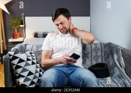 Jeune homme après un accident de voiture souffrant à la maison. Homme en mousse col cervical lisant le message sur le téléphone cellulaire, sensation de douleur dans le cou. Gars portant le cou brac Banque D'Images